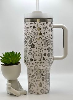 a coffee cup next to a potted plant on a white table with black and white designs