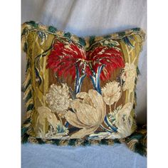 a decorative pillow with red flowers and green leaves on the front, sitting on a blue blanket