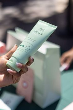 a hand holding a Rael product in a green bottle Exfoliating Cleanser