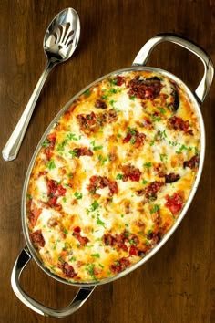 a casserole with meat and cheese in a pan next to a spoon on a wooden table