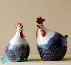 two ceramic roosters sitting on top of a wooden table next to eachother