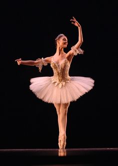 the ballerina is dressed in white and gold, with her arms stretched out to the side