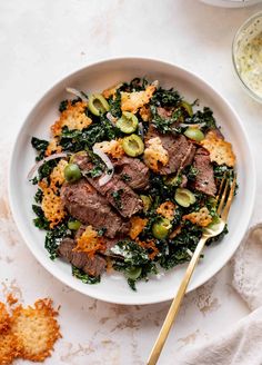 a white bowl filled with meat and vegetables next to crackers on a table top