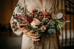 a woman holding a bouquet of flowers and greenery in her hands, close up