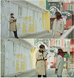 two people standing in front of a wall with writing on it and talking to each other