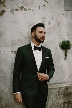 a man in a tuxedo standing against a wall