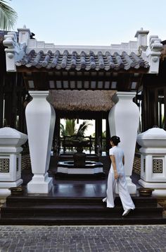 a woman is walking in front of a gazebo with white pillars and columns on either side