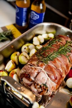 a large piece of meat sitting on top of a pan filled with apples and onions