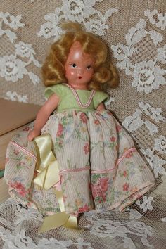 a doll sitting on top of a table next to a book and lace covered wall