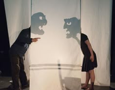 a man and woman standing in front of a white screen with shadows on it, facing each other