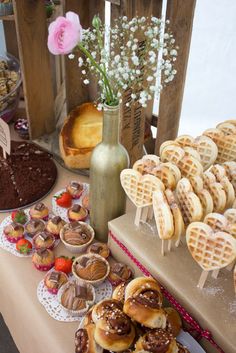 a table topped with lots of different types of pastries next to a vase filled with flowers