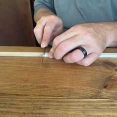 a man is using a pair of scissors to cut the edge of a piece of wood