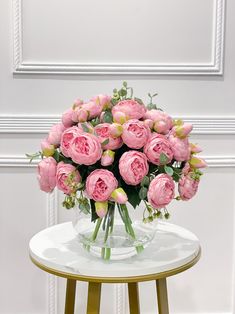 a vase filled with pink flowers sitting on top of a table next to a white wall