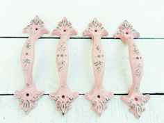 three pink iron door handles on a white painted wood surface with flowers and leaves drawn on them