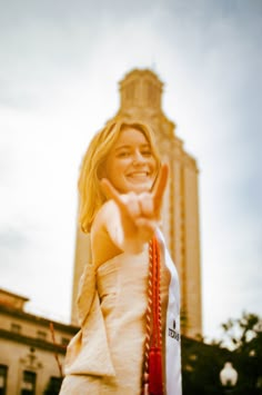 a woman in a white dress pointing at the camera with a building in the background