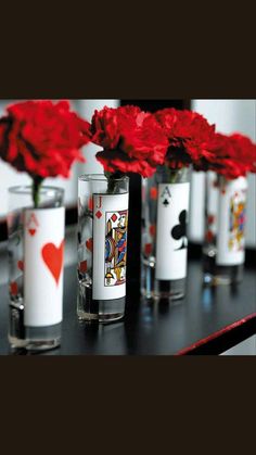 several vases filled with red flowers and playing cards