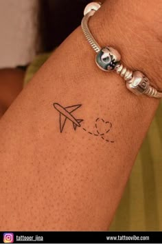 a woman's arm with a tattoo on it and an airplane flying above the clouds