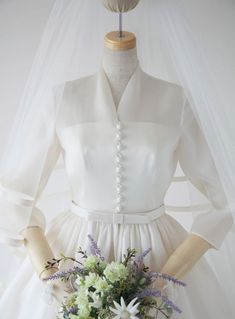 a white dress with flowers on it and a veil hanging from the neckline, in front of a mannequin