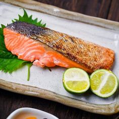 a piece of salmon on a platter with limes and sauce