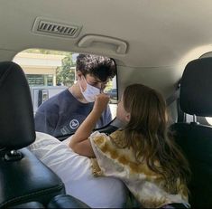 two children sitting in the back seat of a car, one is wearing a face mask