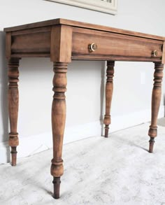 a wooden table with two legs and a drawer on the top, in front of a white wall