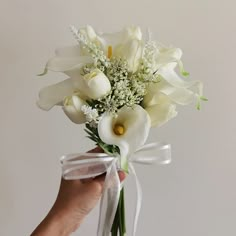 a person holding a bouquet of white flowers in their left hand with a ribbon around it