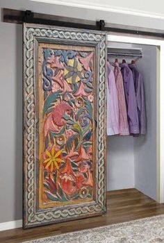 an ornately decorated door is open to reveal a closet with clothes on hangers