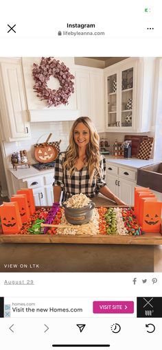 a woman standing in front of a table with halloween decorations on it and pumpkins around her