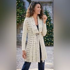 a woman standing in front of a christmas tree wearing a white crocheted cardigan