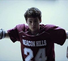 a young man in a maroon jersey holding his arms out and looking at the camera