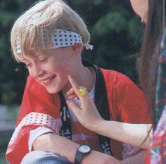 a young boy sitting on the ground with his hand to his face and another person standing behind him