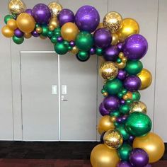 an arch made out of balloons in the shape of a wreath with gold, green and purple balls