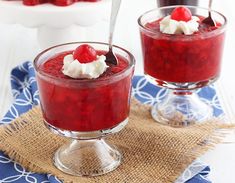 two desserts with cherries and whipped cream in small glass dishes on a table