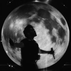 a man standing in front of a full moon with his arms spread out to the side