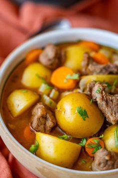 a white bowl filled with stew and potatoes on top of a red cloth next to a spoon