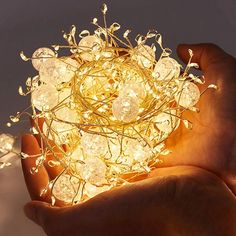 a hand holding a string light with small white balls in the center and gold wire around it