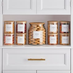 jars filled with food sitting on top of a white shelf next to cabinets and drawers