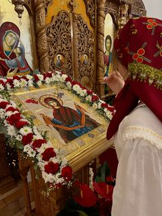 a woman kneeling down in front of a table with flowers and an icon on it