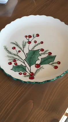 a white plate with holly and red berries on it sitting on top of a wooden table