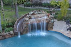 a backyard pool with waterfall and patio furniture