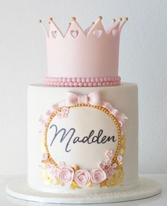 there is a white cake with pink and gold decorations on the top, along with a crown