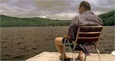 a man sitting in a chair on top of a pier next to the ocean under a cloudy sky