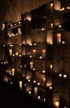 rows of lit candles are lined up against a wall