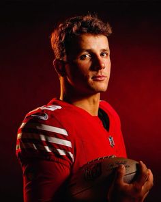 a man in a red jersey holding a football and looking at the camera with a serious look on his face