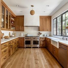 a large kitchen with wooden cabinets and white counter tops, hardwood flooring, and an open window