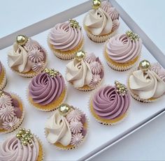 twelve cupcakes with pink and white frosting in a box on a table