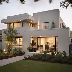 a large white house with lots of windows and plants in the front yard at dusk