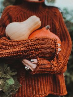 a woman in an orange sweater holding a pumpkin and a white acorn on her arm