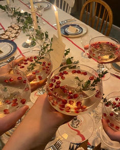 several people holding wine glasses filled with liquid and garnished with greenery on the table