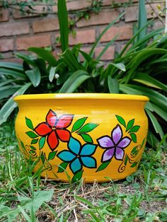 a yellow flower pot sitting on the ground in front of some grass and plants with flowers painted on it